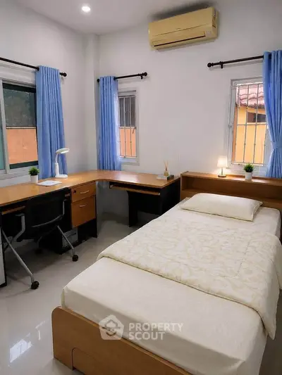 Cozy bedroom with study area, featuring a single bed, desk, and natural light from two windows.