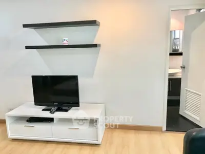 Modern living room with sleek TV stand and floating shelves, adjacent to a bathroom entrance.
