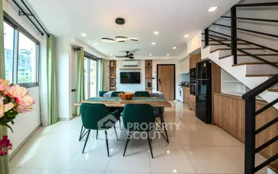 Modern open-plan living room with stylish dining area and staircase, featuring elegant decor and ample natural light.