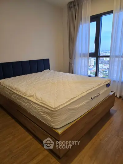 Spacious bedroom with large window offering stunning city views, featuring a comfortable bed and elegant wooden flooring.