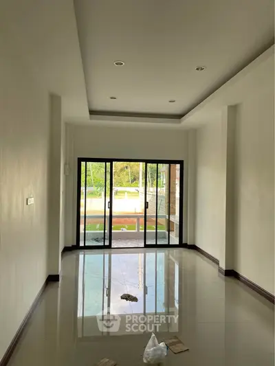 Spacious empty room with large sliding glass doors and glossy tiled floor