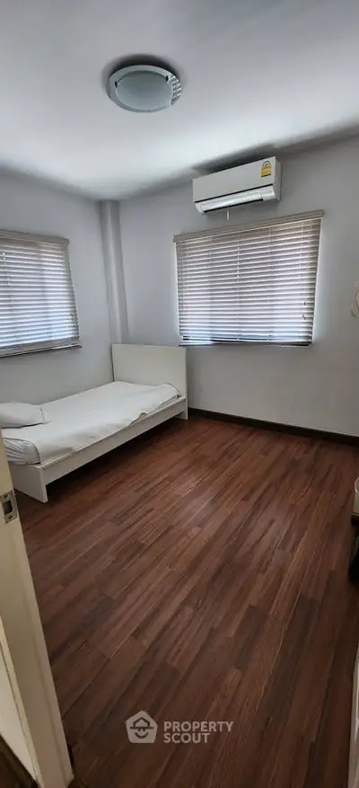 Cozy bedroom with wooden flooring and air conditioning, perfect for a comfortable living experience.