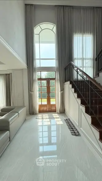 Luxurious high-ceiling living room with elegant staircase and large window