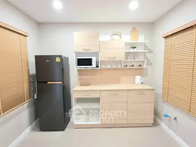 Modern kitchen with sleek cabinets, fridge, microwave, and kettle in a bright, minimalist design.