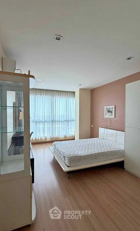 Spacious bedroom with large window and modern furnishings in a stylish apartment.