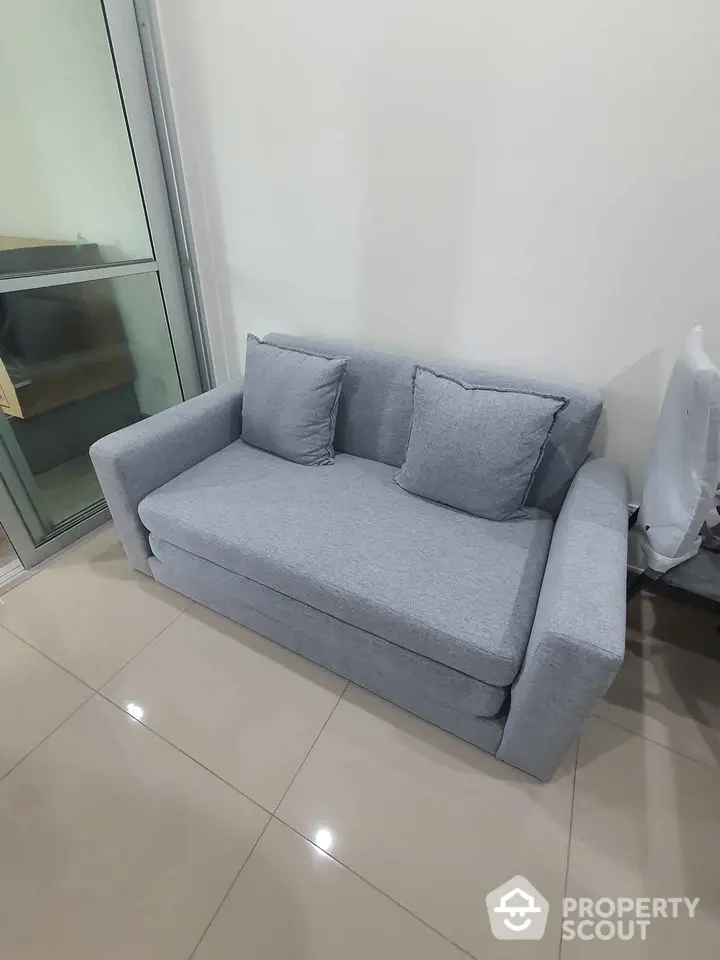 Modern gray sofa in a stylish living room with glossy tiled flooring and glass door.