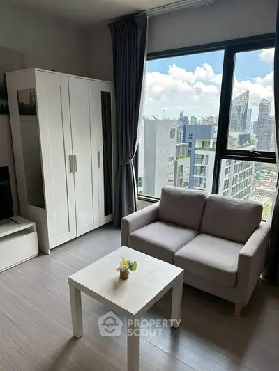 Modern living room with city view, featuring a cozy sofa, sleek white furniture, and large windows.