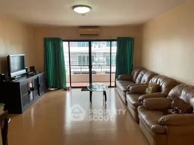 Spacious living room with leather sofa and balcony view, perfect for relaxation.