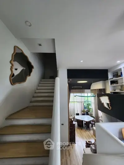 Modern open-plan living room with stylish staircase and large windows for natural light.