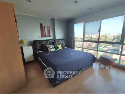 Spacious bedroom with large windows offering city views, featuring a stylish bed and modern decor.
