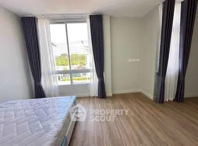 Spacious bedroom with large windows and elegant curtains, showcasing natural light and modern flooring.
