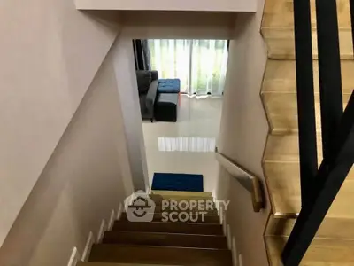 Modern staircase leading to a bright living area with large windows and stylish decor.