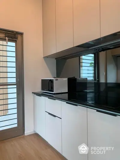 Sleek modern kitchen with high-gloss white cabinetry and black countertops, featuring built-in appliances and a view to the outdoors through a glass door.