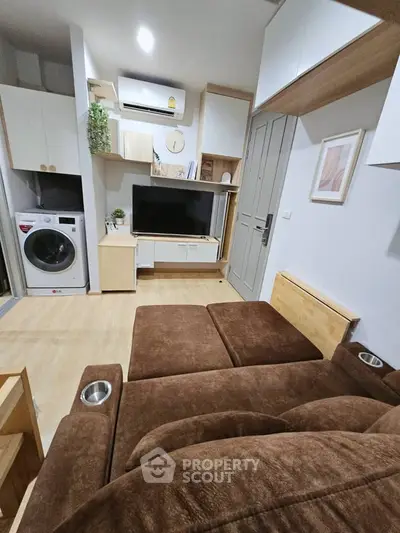 Modern living room with cozy brown sofa, TV, and built-in storage, featuring a washing machine and air conditioning.
