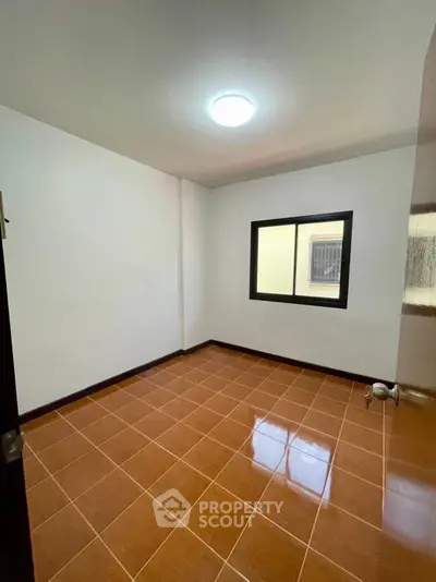 Spacious empty room with tiled floor and window, perfect for customization.