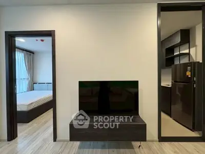 Modern apartment interior with sleek TV setup and view into bedroom and kitchen.