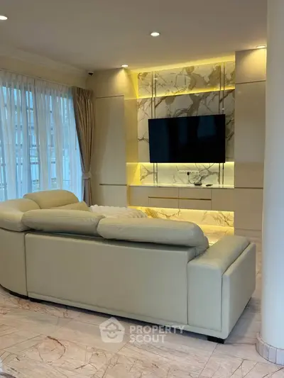 Luxurious living room with elegant marble accents and modern lighting, featuring a plush sofa and large TV.