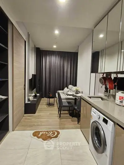 Modern open-layout living room with kitchen, featuring sleek design and integrated washing machine.
