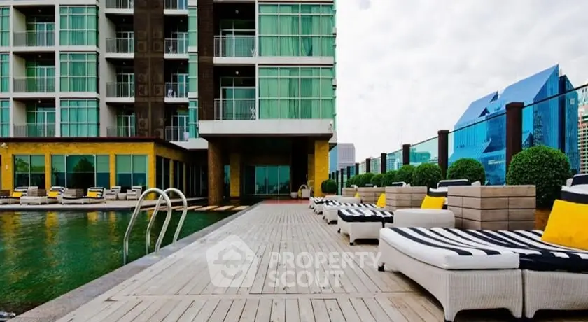 Luxurious poolside view at modern apartment complex with stylish loungers and cityscape backdrop.