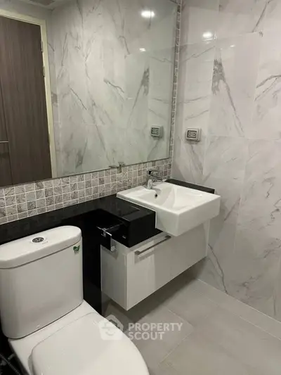 Modern bathroom with sleek fixtures and marble tiles, featuring a stylish sink and toilet.