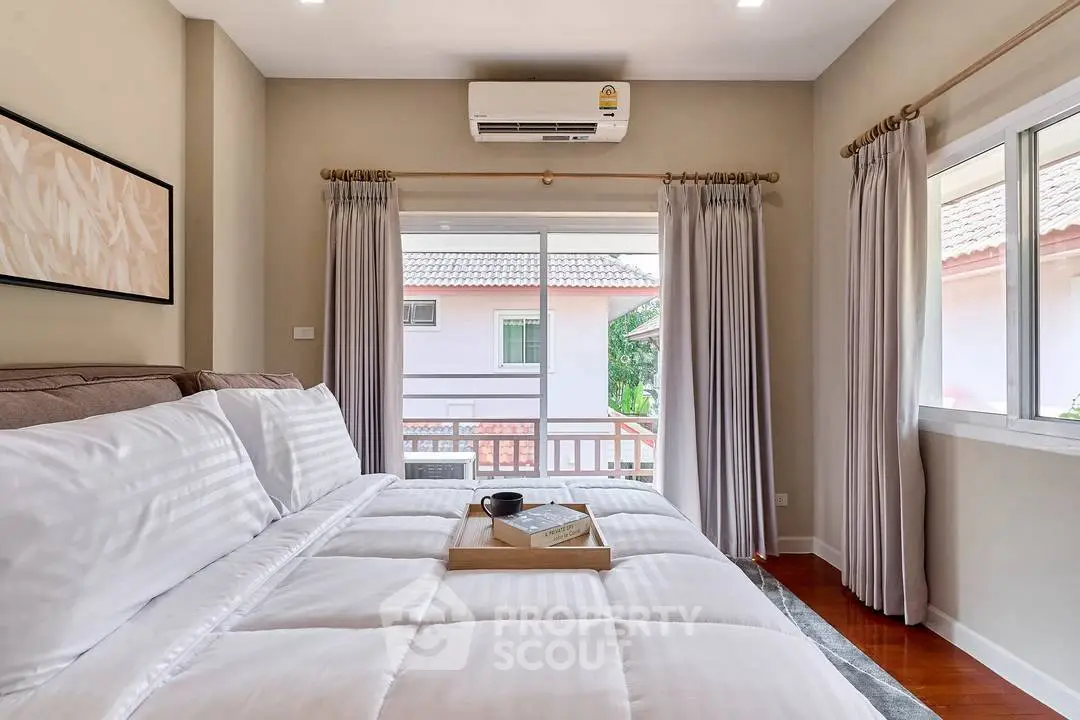 Spacious bedroom with cozy bedding and natural light from large window, perfect for relaxation.