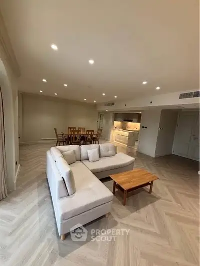 Spacious modern living room with open kitchen and elegant dining area, featuring stylish furniture and lighting.