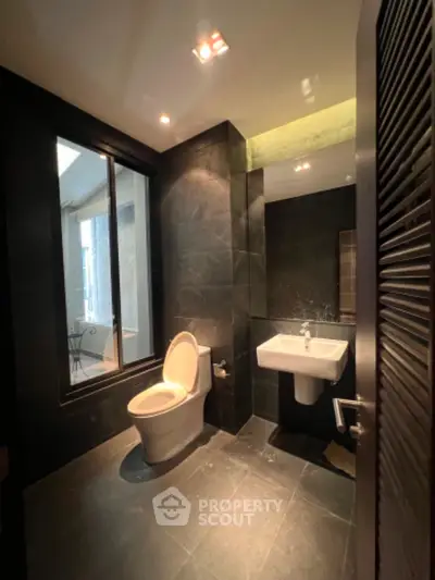 Modern bathroom with sleek dark tiles, featuring a large window offering natural light and a view of the outdoor terrace.