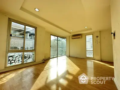 Spacious sunlit living room with large windows and wooden flooring