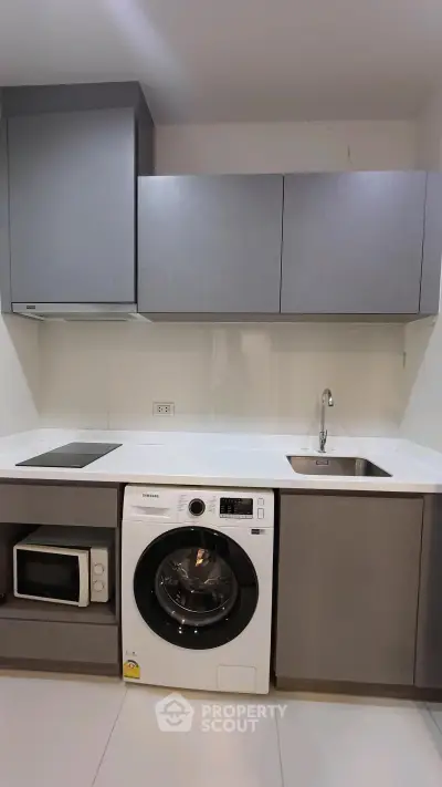 Modern kitchen with sleek cabinets, washing machine, and microwave in a compact layout.