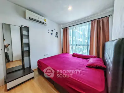 Cozy bedroom with vibrant red bedding and modern decor, featuring a large window for natural light.