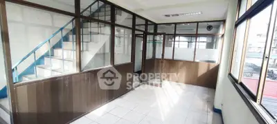 Spacious office space with large windows and natural light, featuring a staircase and glass partitions.