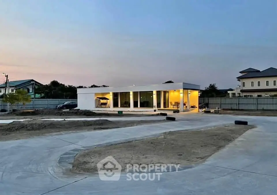 Modern minimalist house with large windows and spacious driveway at dusk.