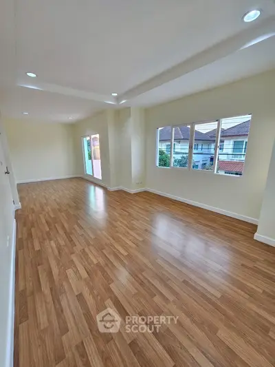Spacious empty room with wooden flooring and large windows offering natural light.