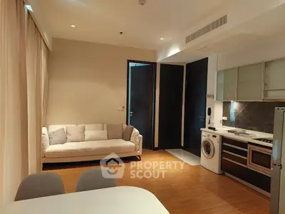 Modern open-layout living room with kitchen, featuring a cozy sofa and built-in appliances.