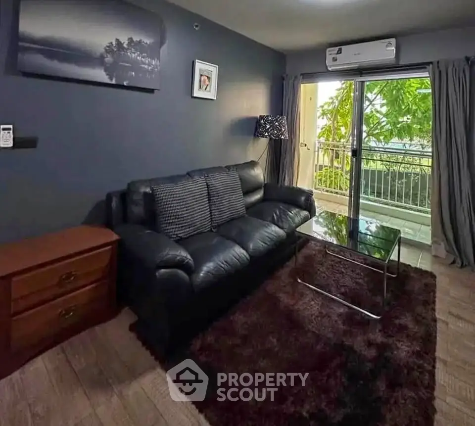Cozy living room with black leather sofa, glass coffee table, and balcony view.