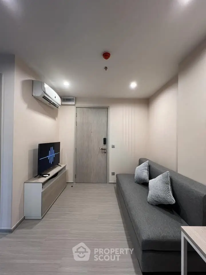 Modern living room with sleek gray sofa, wall-mounted TV, and minimalist decor.