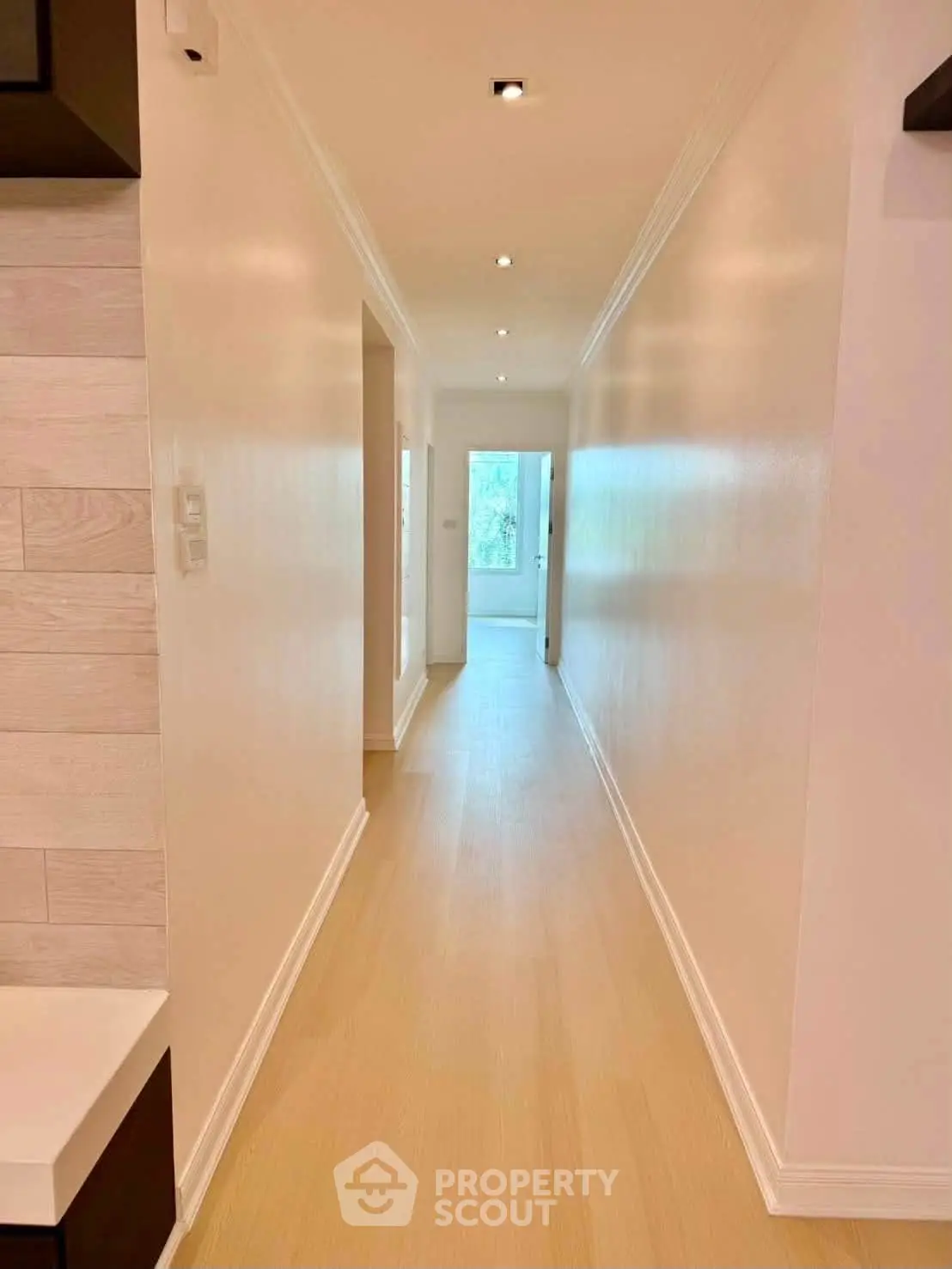 Bright hallway with wooden flooring leading to a sunlit room, showcasing modern interior design.