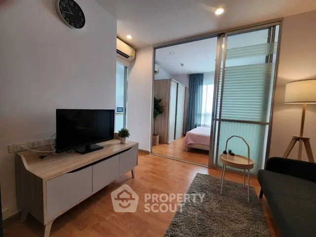 Modern living room with TV, cozy seating, and view into a stylish bedroom