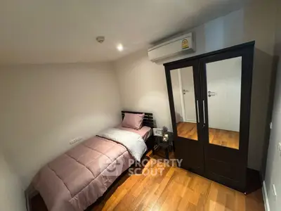 Cozy bedroom with single bed and mirrored wardrobe, featuring wooden flooring and air conditioning.