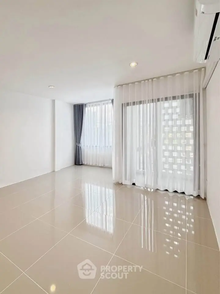 Spacious empty room with glossy tiled floor and large windows with sheer curtains.