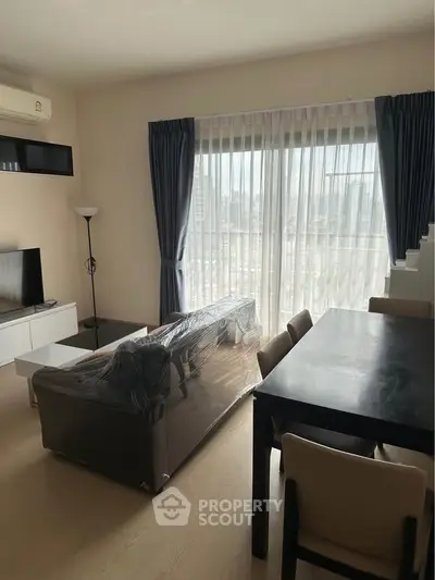 Modern living room with city view, featuring a sleek sofa, dining table, and large windows with curtains.