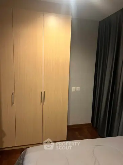 Cozy bedroom with wooden wardrobe and elegant curtains, perfect for a restful retreat.