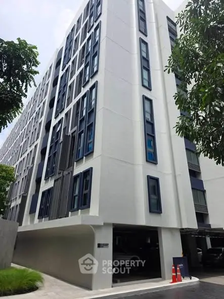 Modern multi-story residential building with sleek design and parking area.