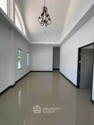 Spacious empty room with high ceiling and elegant chandelier, perfect for customization.