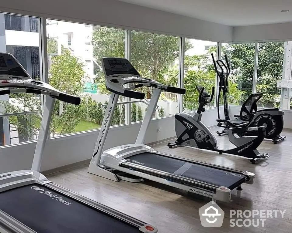 Modern gym with state-of-the-art equipment and large windows offering a lush garden view.