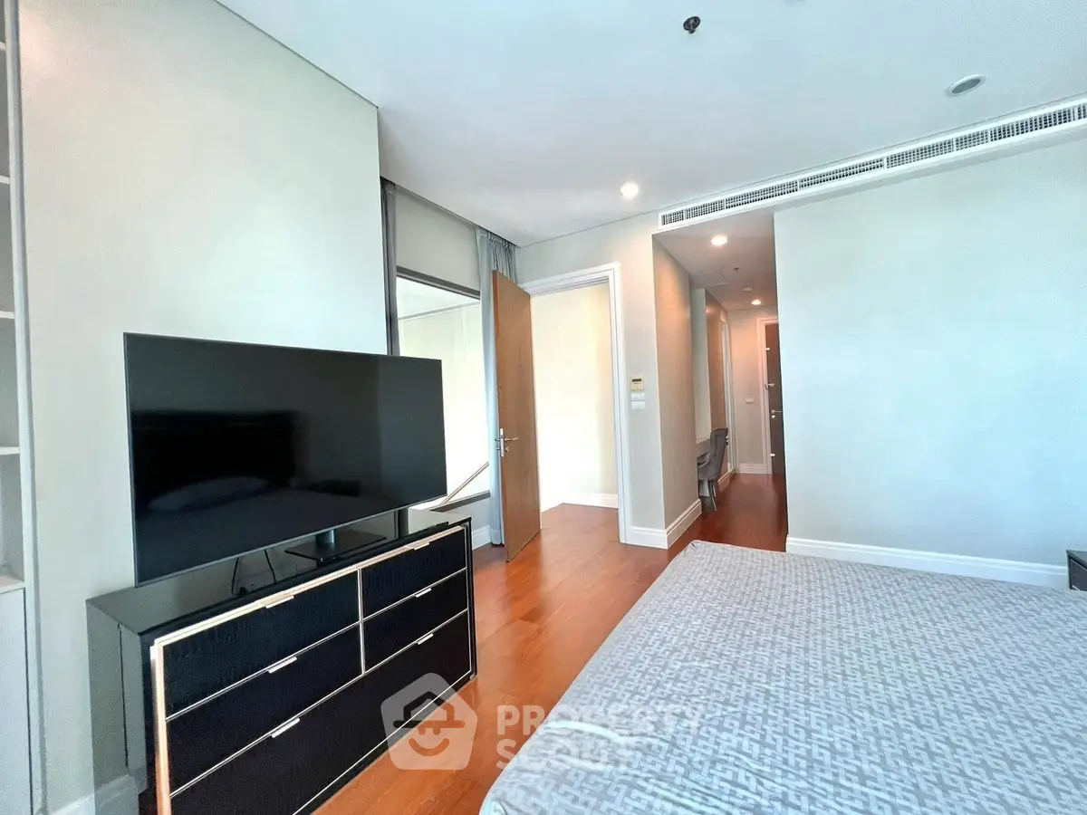 Spacious modern bedroom with sleek TV setup and elegant wooden flooring.