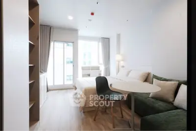 Modern studio apartment with cozy bed, stylish sofa, and natural light from large window.