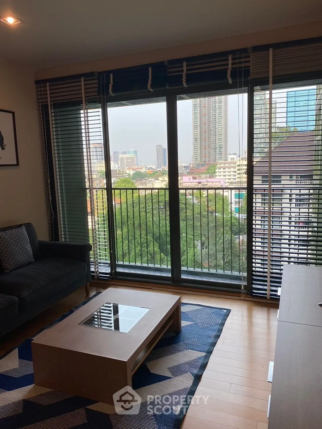 Modern living room with large windows offering a stunning city view, featuring stylish furniture and wooden flooring.