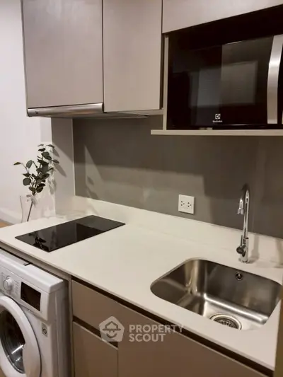 Modern kitchen with sleek appliances and compact design, featuring a washing machine and microwave.