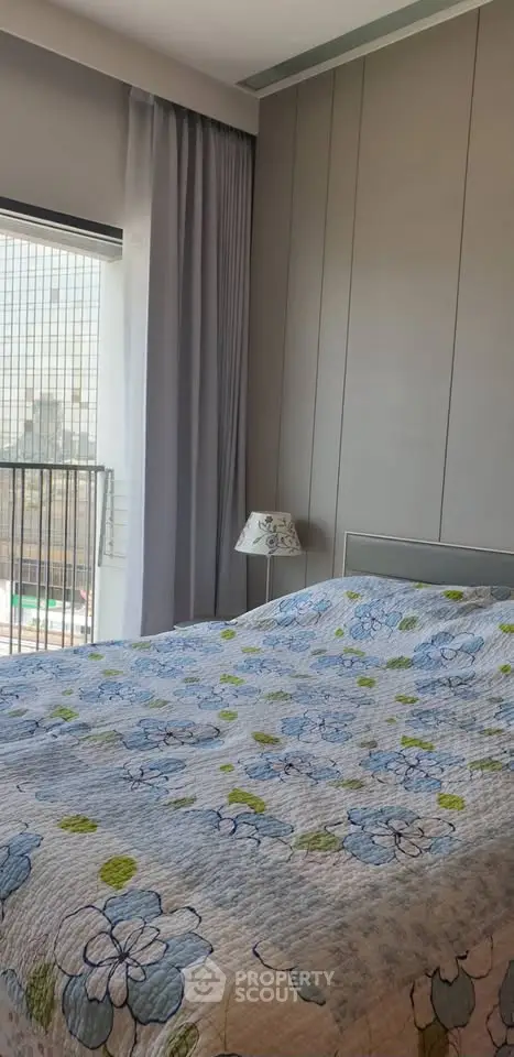 Cozy bedroom with floral bedding and city view from window, perfect for urban living.